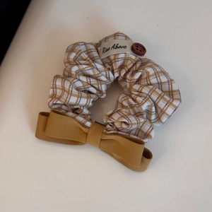 Macro detail of plaid fabric scrunchie with yellow bow and vintage brown button