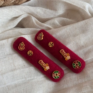 Detail of red felt hair clips with golden lucky charms and Rich letter tag on linen cloth