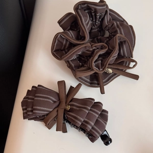 Dettaglio di elastico e molletta a righe marroni con logo dorato su sfondo in pelle