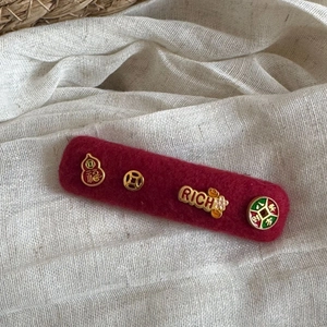 Detailed macro of red felt hair clip featuring gold lucky charms and festive symbols