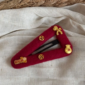 Detailed view of dark red felt hair clip featuring gold Rich lettering and lucky coin symbols