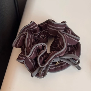 Dettaglio di uno scrunchie retrò a righe con bordo grigio e piccolo ciondolo dorato
