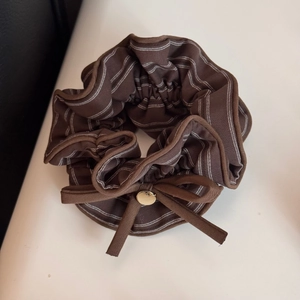 Dettaglio dell'elastico scrunchie marrone a righe con fiocco e ciondolo dorato