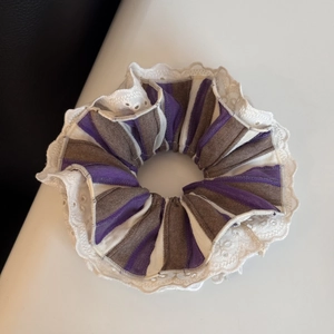 Dettaglio di un elastico per capelli a righe con bordo in pizzo bianco viola e grigio