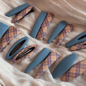 Detailed view of plaid and solid blue fabric covered hair clips on beige linen fabric