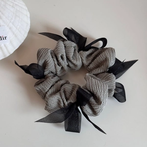 Detail of grey striped fabric scrunchie with a black chiffon bow on a white background