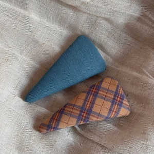 Close-up of fabric plaid and denim blue triangle hair clips on a linen surface