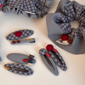 Detailed view of gray fabric scrunchies and plaid hair clips set with heart and bear charms