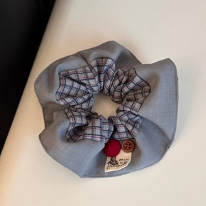 Detail of grey fabric scrunchie with plaid pleats, wood button and handmade bear label