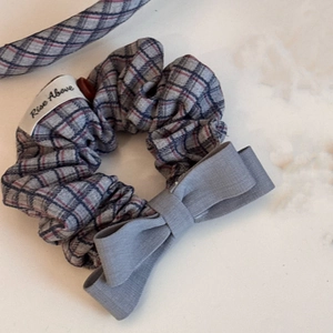Detail of grey plaid hair scrunchie with Rise Above tag and elegant bow accessory