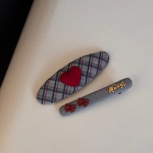 Detail of fabric hair clips with blue plaid heart and red bow on ribbed grey textile