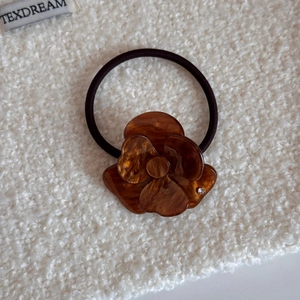 Dettaglio dell'elastico per capelli con fiore in acetato marrone e trama ambrata con strass