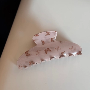 Gros plan d'une pince à cheveux mate rose avec des motifs de papillons marron