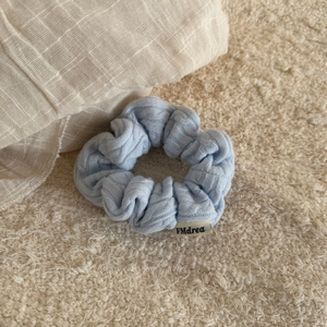 Detail of light blue textured fabric scrunchie with woven label on a soft textile background