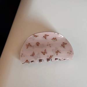Vue détaillée d'une pince à cheveux rose en acétate avec motifs papillon violets