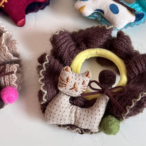 Detail eines gestrickten Haargummis mit beigem Stoff-Katzenanhänger und Plüschball