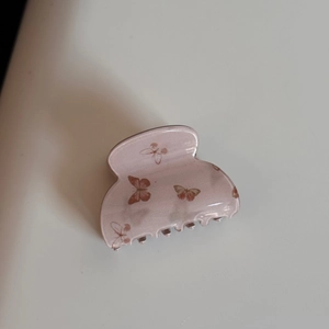 Gros plan d'une pince à cheveux rose poudré avec motif de papillons sur fond blanc