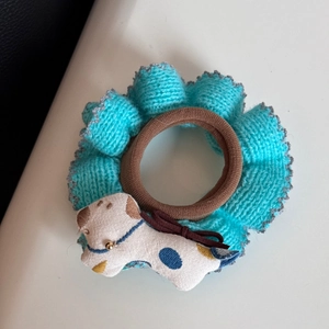 Detail eines braunen Scrunchies mit blauem Strickrand und süßem Welpen-Plüschanhänger