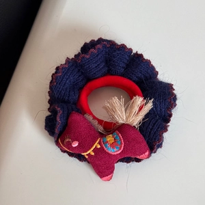 Detailansicht eines gestrickten Haargummis mit besticktem Pony-Anhänger und gelber Quaste