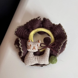 Detail eines Strick-Haargummis mit Katzen-Stickerei und grünem Plüschball-Dekor