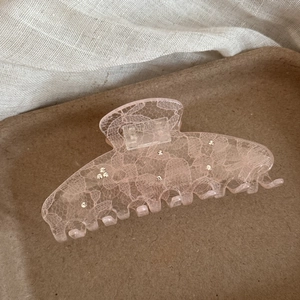 Detail of pink lace hair claw clip with rhinestones on a textured beige background