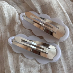Detail view of cloud-shaped white hair clips with wavy plastic edges and metal snap-on grips