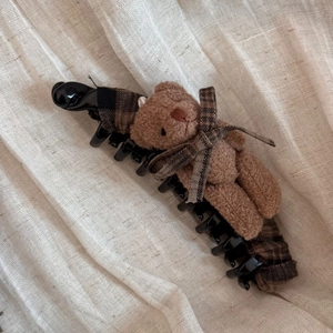 Dettaglio del fermaglio a banana con orsetto di peluche marrone e fiocco a scacchi