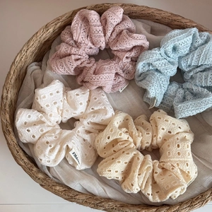 Detail of four hollow lace scrunchies in soft Morandi colors placed in a woven basket
