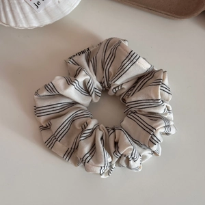 Detail of cream striped fabric scrunchie with soft pleats and brand label on white surface