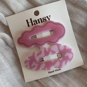 Detail view of two wavy handmade hair clips in pink and marble patterns on a display card