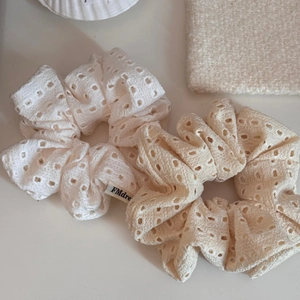 Close-up of lace scrunchies in white and beige with delicate cutout floral patterns