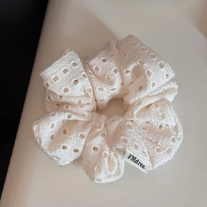 Detailed close-up of white embroidered lace scrunchie with a woven logo tag on white