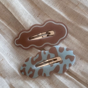 Close-up of leopard print and mocha wave hair clips on textured cream fabric
