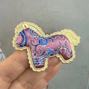 Close-up detail of the Song brocade horse brooch featuring an ornate scalloped border.