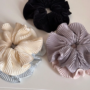 Macro detail of assorted pleated satin scrunchies showing glossy fabric texture and elastic design
