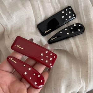 Elegant red and black rhinestone hair clips with gold Nuance branding on beige fabric