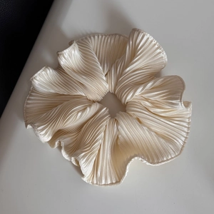 Detailed view of large cream pleated scrunchie with satin texture and vertical ruffles