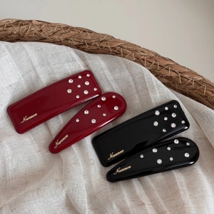 Elegant red and black hair clips with gold label and sparkling rhinestones on white fabric