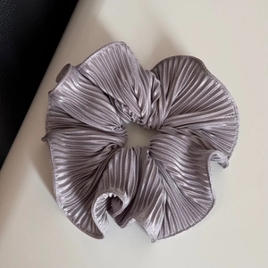 Detailed view of silver pleated satin scrunchie with metallic sheen and elastic texture
