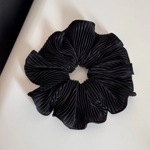 Detailed macro view of large black pleated scrunchie with glossy ruffled fabric texture