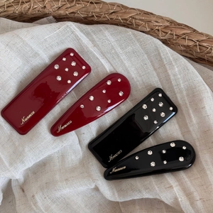 Detail of red and black resin hair clips with rhinestones and golden Nuance text