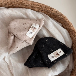 Detail of floral baby knit hats in beige and dark grey with cute bear logo on white labels