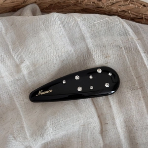 Detail of a black teardrop hair clip with rhinestones and gold Nuance lettering