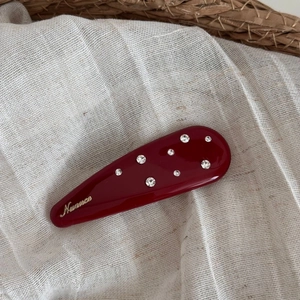 Macro shot of a dark red rhinestone hair clip with gold logo on natural linen