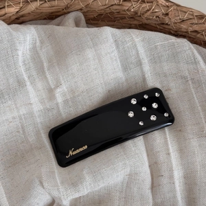 Detailed close-up of a black resin hair clip with gold Nuance lettering and rhinestones