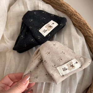 Detail of floral knit beanies with plush teddy bear labels on rustic linen fabric