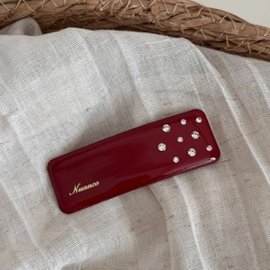 Detail of a red enamel rectangular hair clip with gold Nuance logo and rhinestones