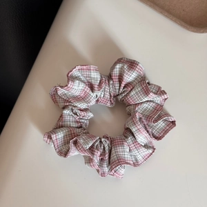 Nahaufnahme des rosa-weiß karierten Stoff-Haargummis mit weicher Rüschendekoration