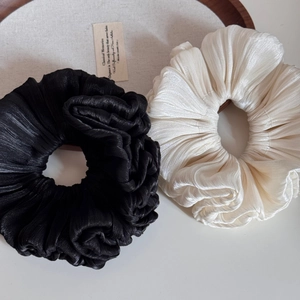 Macro detail of pleated satin scrunchies in black and champagne white with elegant texture