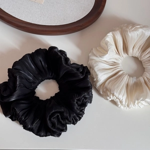 Detailed macro shot of pleated satin scrunchies in black and cream with a silk texture